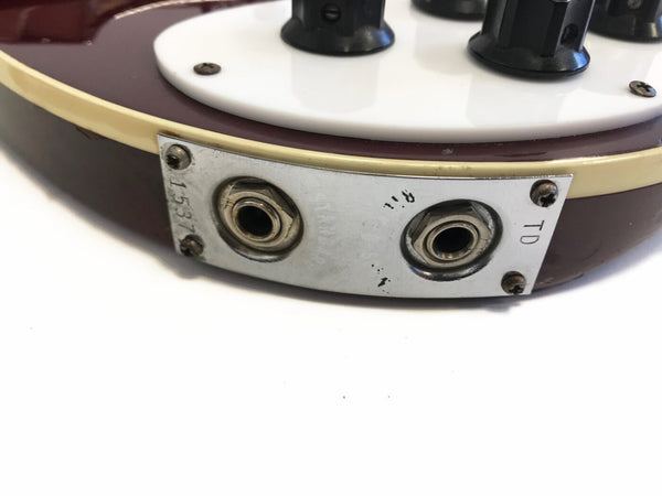Close-up of metal input jack plate with two jacks on vintage electric guitar body with cream binding and white pickguard.