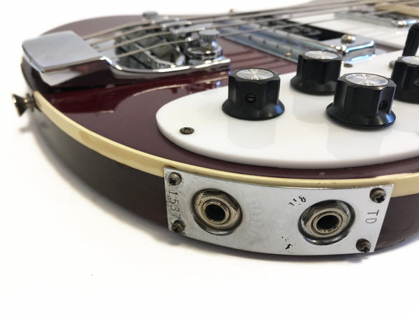 Close-up of electric guitar input jack plate with two 1/4 inch input jacks and black control knobs on white pickguard.