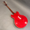 Back view of red semi-hollow electric guitar with wooden neck and cream binding on gray surface