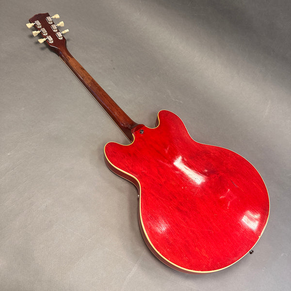 Back view of red semi-hollow electric guitar with wooden neck and cream binding on gray surface