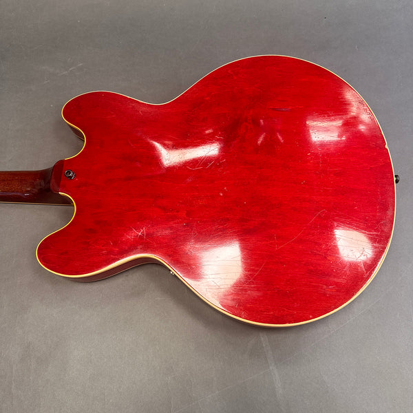 Back of vintage red semi-hollow electric guitar with cream binding and visible wear and scratches on gray background