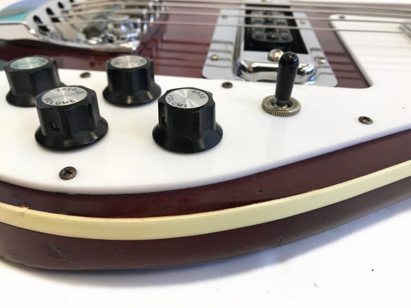 Close-up of black volume and tone control knobs and pickup selector switch on vintage electric guitar with white pickguard and cherry red body.