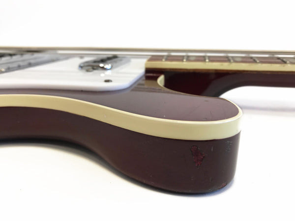 Close-up of vintage burgundy electric guitar body with cream binding and white pickguard showing wear and scratches on finish