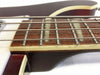 Close-up of electric bass guitar fretboard with metal frets, pearl inlays, and wound strings, featuring cream binding and dark wood grain fingerboard.