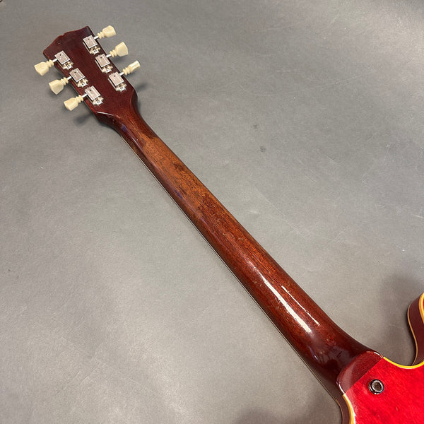 Back of guitar neck and headstock with vintage tuning pegs on brown guitar neck against gray background