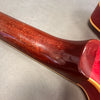 Close-up of the worn back neck and heel of a vintage guitar with reddish-brown wood finish and cream binding on a grey surface