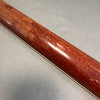Close-up of worn and scratched back of guitar neck with reddish wood finish on gray surface