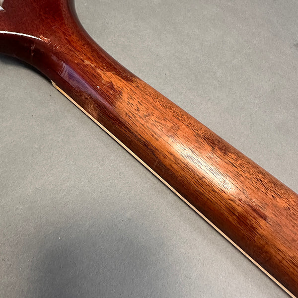 Close-up of polished mahogany guitar neck with natural wood grain texture on gray background