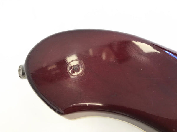 Close-up of deep red glossy electric guitar body with strap button and visible screw indentation on white background
