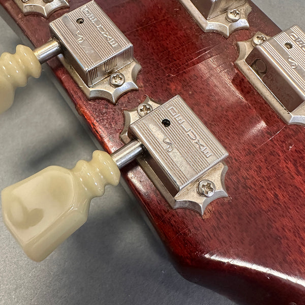 Close-up of vintage guitar tuning pegs with cream plastic keys on a worn red wooden guitar headstock featuring Maxcap brand metal tuners