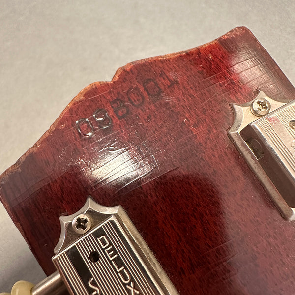 Close-up of vintage Gibson Deluxe tuners on worn cherry red guitar headstock with visible serial number and finish wear