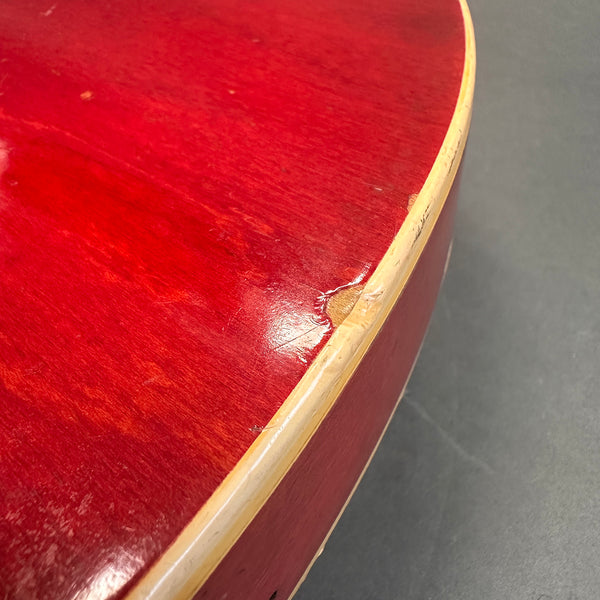 Close-up of red acoustic guitar body edge with visible chip and wear on cream binding, showcasing vintage guitar condition.