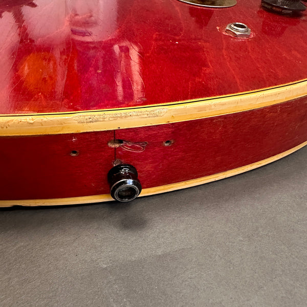 Close-up of red electric guitar body edge with worn finish and missing control knob on grey surface