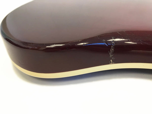Close-up of brown electric guitar body edge showing white binding and wear damage on the finish