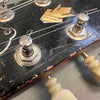 Close-up of vintage guitar headstock showing tuning pegs, worn black finish, and mother of pearl inlay detail