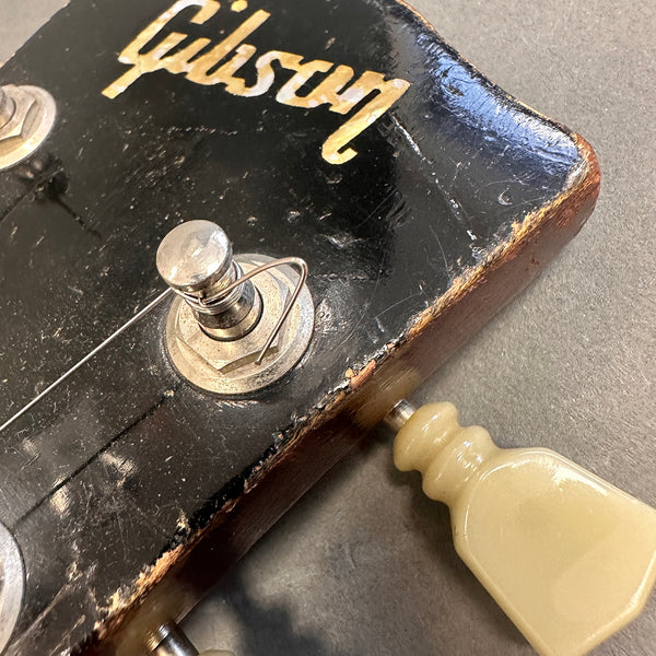 Close-up of worn black Gibson guitar headstock with tuning peg and string wound around post