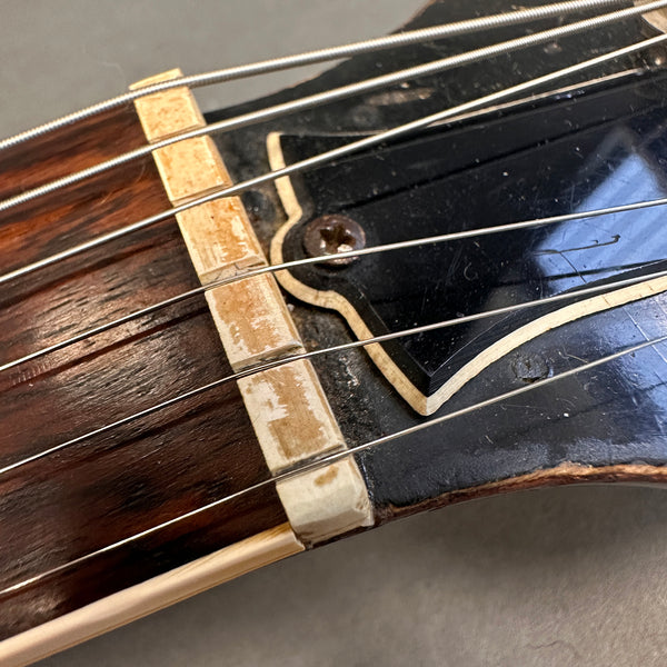 Close-up of worn guitar nut and steel strings on vintage acoustic guitar with black headstock and visible screw detail