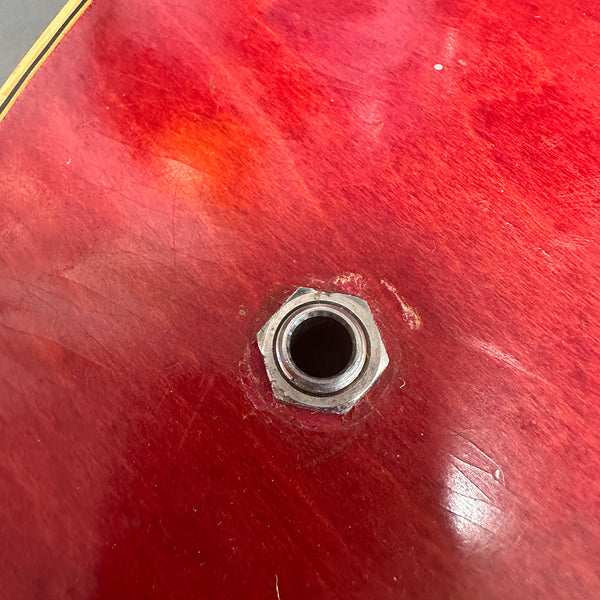 Close-up of red electric guitar body with metal input jack socket and visible wear marks.