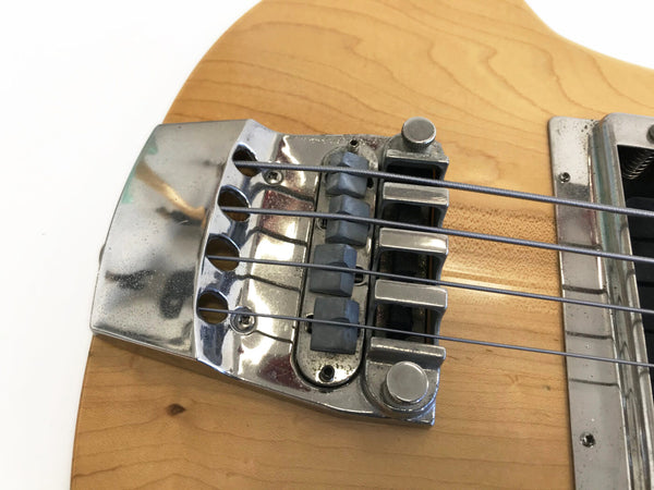 Close-up of vintage electric bass guitar chrome bridge and strings on natural wood finish body