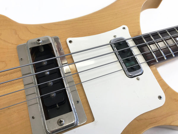 Close-up of natural wood electric bass guitar body showing chrome pickups, white pickguard, and metal strings on fretboard