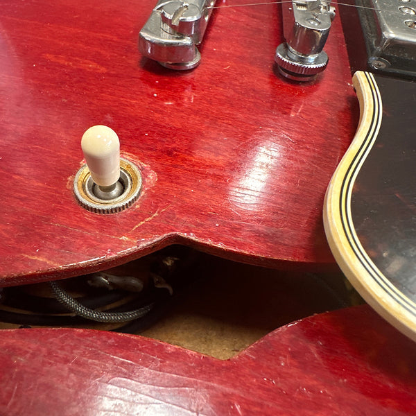 Close-up of red electric guitar body showing white toggle switch, metal hardware, and wiring cavity with visible wear and scratches
