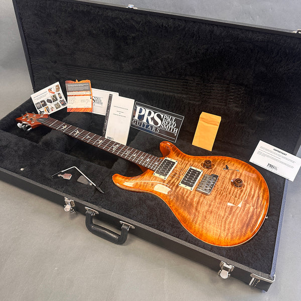 Paul Reed Smith PRS electric guitar with flame maple top in open black hard case, including tremolo arm, PRS logo sticker, manuals, and warranty cards