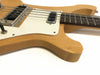 Close-up of natural finish electric bass guitar body showing white pickguard, pickups, and four strings on white background