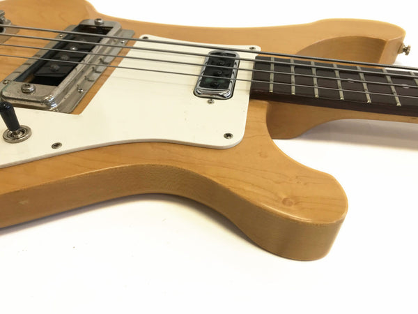 Close-up of natural finish electric bass guitar body showing white pickguard, pickups, and four strings on white background