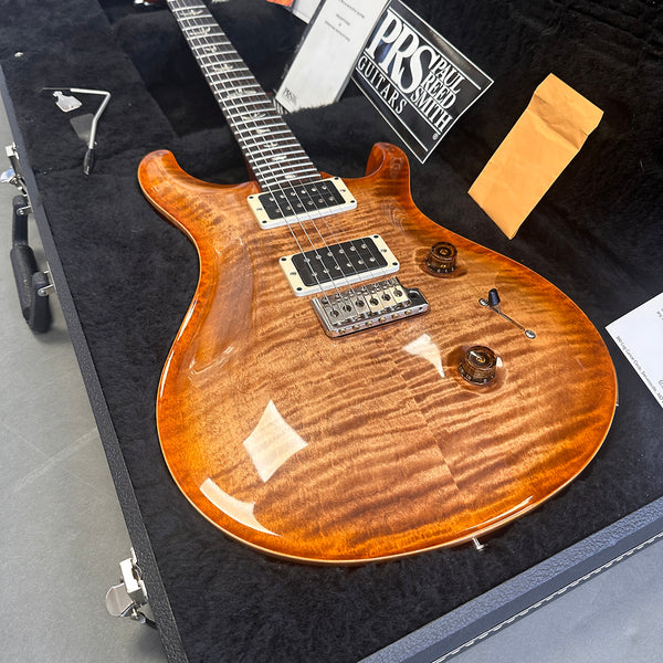Paul Reed Smith PRS electric guitar with flame maple top in amber finish, displayed in black plush guitar case with accessories and PRS certification.