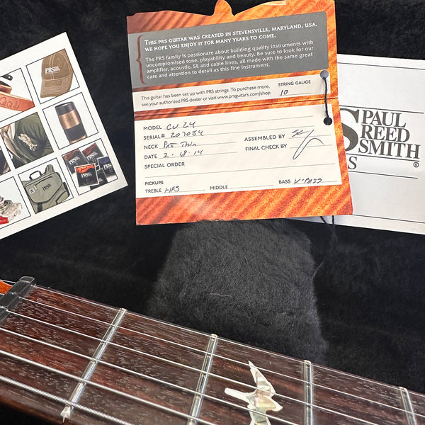 Close-up of Paul Reed Smith PRS guitar certificate of authenticity with model CU 24 and serial number 207054, set on black plush background next to guitar fretboard with bird inlay and several PRS promotional cards