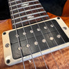 Close-up of electric guitar pickup and strings on wood finish guitar body with pearl inlay fretboard