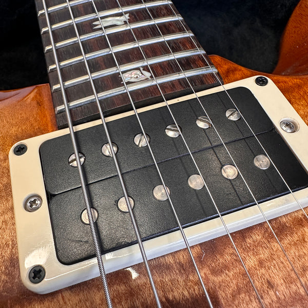 Close-up of electric guitar pickup and strings on wood finish guitar body with pearl inlay fretboard