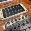 Close-up of electric guitar bridge and black humbucker pickup on wood grain body with metal strings and adjustment screws