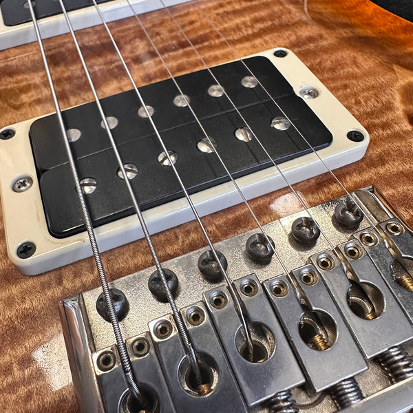 Close-up of electric guitar bridge and black humbucker pickup on wood grain body with metal strings and adjustment screws