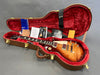 Gibson Les Paul electric guitar in sunburst finish inside brown hardshell guitar case with red plush interior and Gibson documentation