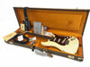 Vintage Fender Stratocaster electric guitar in white with tortoiseshell pickguard, displayed in open brown hard case with orange plush interior, including certificate of authenticity, Fender branded guitar strap, amplifier cable, and various Fender accessories and documentation.