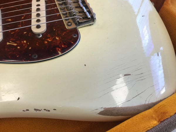 Close-up of vintage cream electric guitar body showing tortoiseshell pickguard, worn paint, and finish checking on lower bout near edge, resting on orange plush-lined case interior