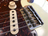 Close-up of electric guitar bridge, pickup, volume knob, and strings on cream-colored body with tortoiseshell pickguard