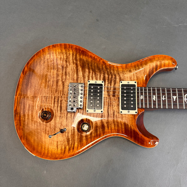 Close-up of electric guitar body with flamed maple top in amber finish, dual humbucker pickups, chrome bridge, volume and tone knobs, and carved cutaway.