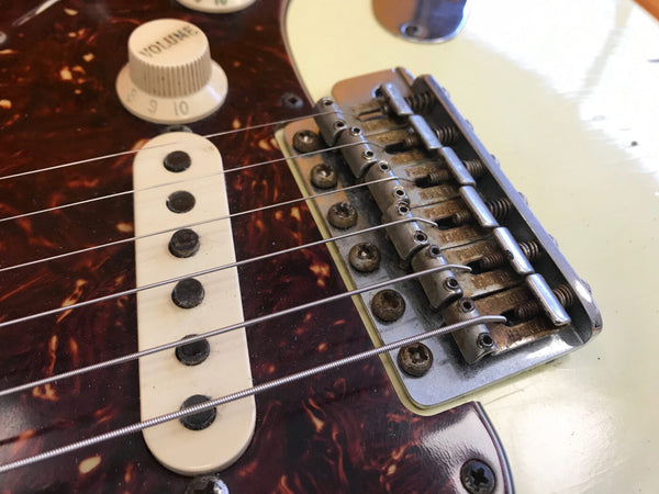 Close-up of electric guitar bridge, pickup, volume knob, and strings on cream-colored body with tortoiseshell pickguard