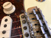 Close-up of Fender electric guitar bridge, volume knob, and single-coil pickup with tortoiseshell pickguard and metal saddle details