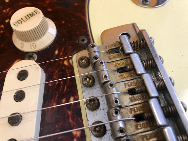 Close-up of Fender electric guitar bridge, volume knob, and single-coil pickup with tortoiseshell pickguard and metal saddle details