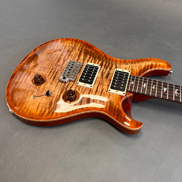Close-up of a glossy amber sunburst electric guitar with dual humbucker pickups, amber control knobs, chrome bridge, and bird inlay fretboard on gray background