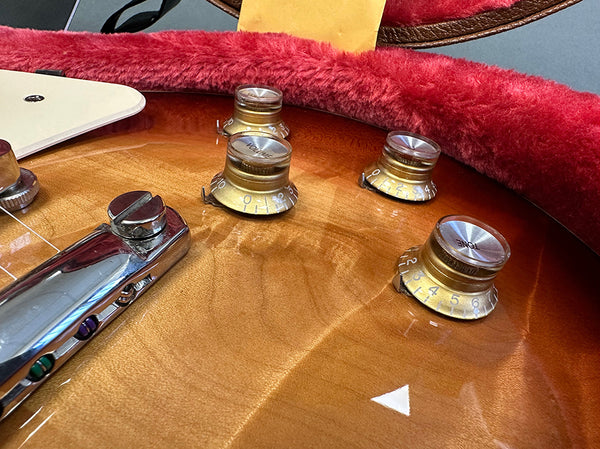 Close-up of vintage sunburst electric guitar body showing gold tone and volume control knobs, chrome bridge, and glossy wood finish with red plush case lining.