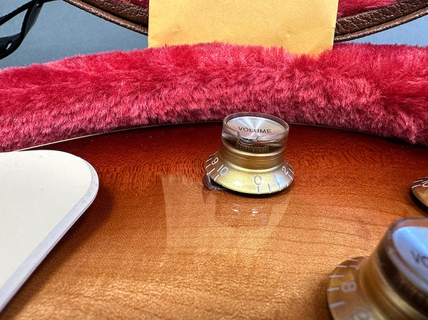 Close-up of volume control knob on amber sunburst electric guitar with plush red-lined case interior in background