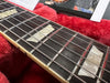 Close-up of electric guitar fretboard with pearloid trapezoid inlays and steel strings resting on red plush guitar case lining