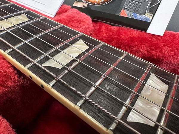 Close-up of electric guitar fretboard with pearloid trapezoid inlays and steel strings resting on red plush guitar case lining