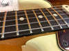 Close-up of electric guitar fretboard with metal frets, dot inlays, and steel strings on a cream-colored body with tortoiseshell pickguard.