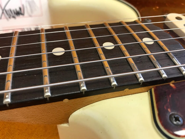 Close-up of electric guitar fretboard with metal frets, dot inlays, and steel strings on a cream-colored body with tortoiseshell pickguard.