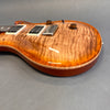 Close-up of electric guitar body with quilted maple top, honey burst finish, two humbucker pickups, chrome bridge, and amber control knobs on grey background